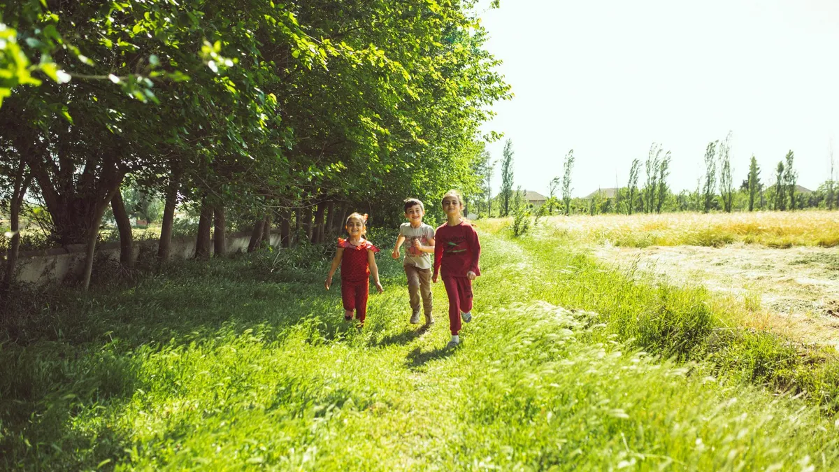 Trois enfants qui courent joyeusement dans un champ ensoleillé